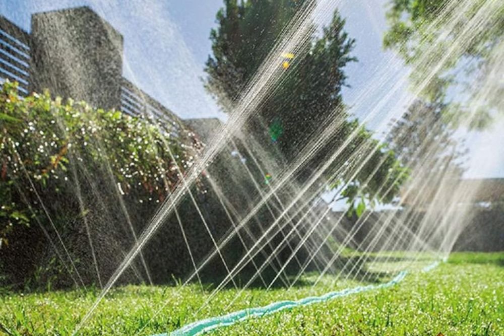 A sprinkler sprays water over a lush green lawn, creating a refreshing mist in the sunlight.
