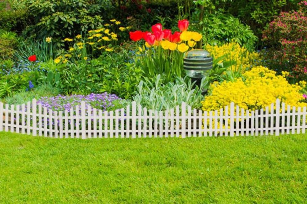 A vibrant garden featuring a white picket fence surrounded by colorful blooming flowers.