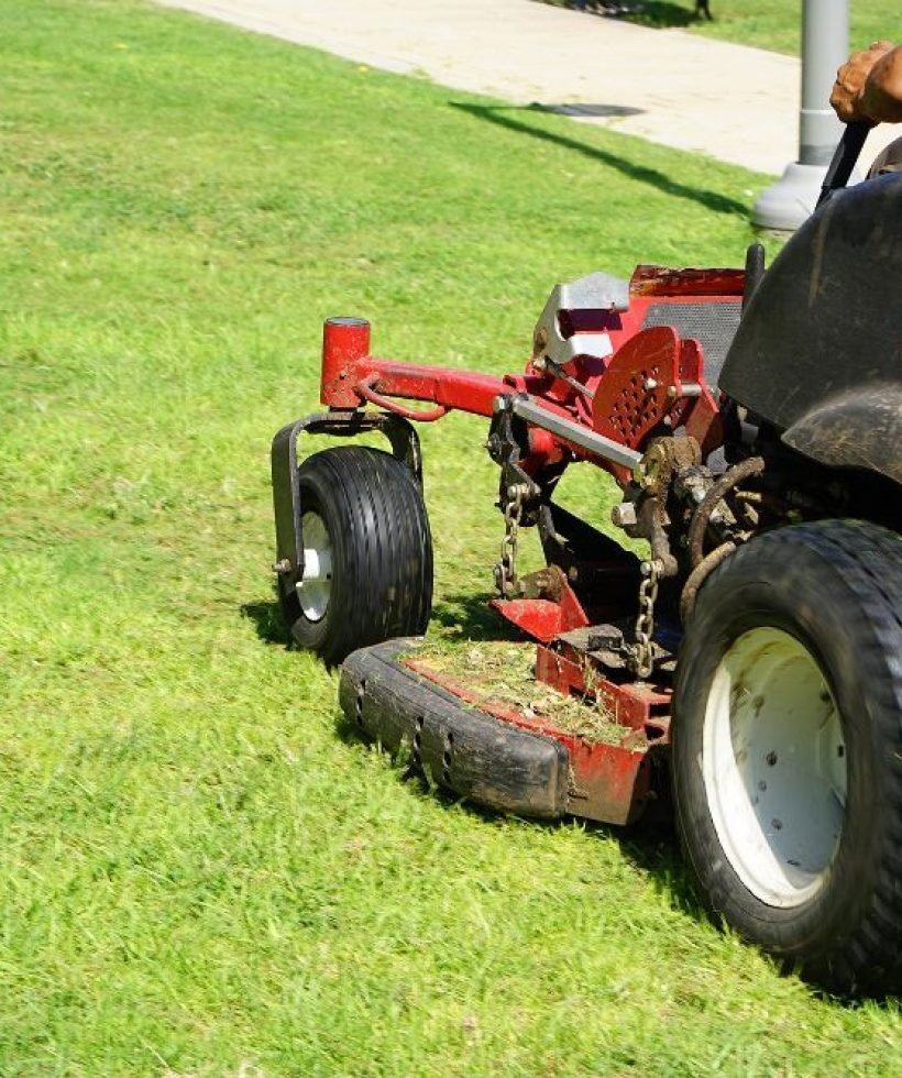 A man using a lawn mower to cut grass on a well-maintained lawn under clear blue skies.